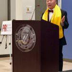 professional man speaking at podium wearing yellow scarf